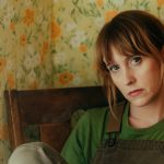 Image of Flock of Dimes sitting in a chair with a floral wallpaper in the background